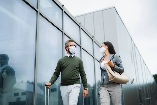 Businesspeople with luggage going on business trip, wearing face masks at the airport. — Stock Photo, Image