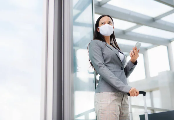 Empresaria con smartphone en viaje de negocios, con mascarillas en el aeropuerto . — Foto de Stock