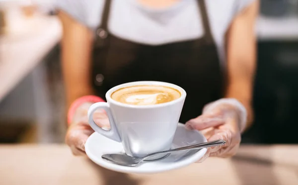 Mujer irreconocible con guantes trabajando en la cafetería, sosteniendo una taza de café . — Foto de Stock