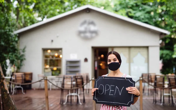 Young woman with face mask working in cafe, holding open sign. — Stock Photo, Image