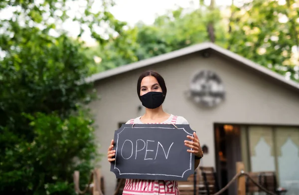 Young woman with face mask working in cafe, holding open sign. — Stock Photo, Image