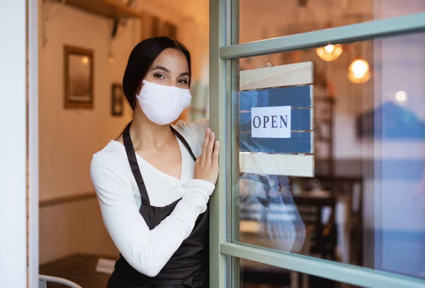 Young waitress with face mask by entrance door in cafe, reopening concept. — Stock Photo, Image