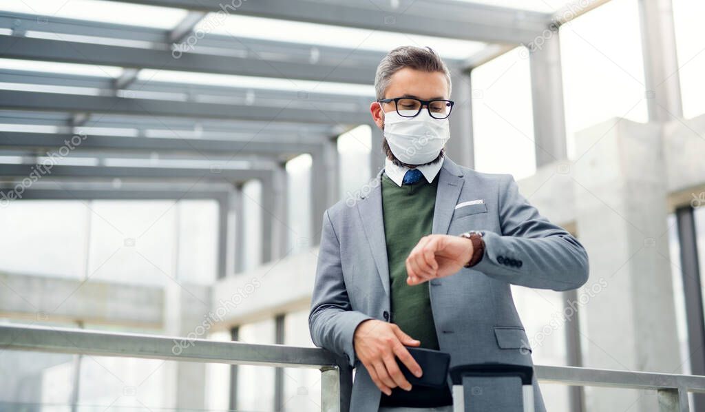 Businessman with face mask going on business trip, checking the time at the airport.