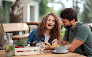 Teras restoranında oturan mutlu çift akıllı telefon kullanıyor..