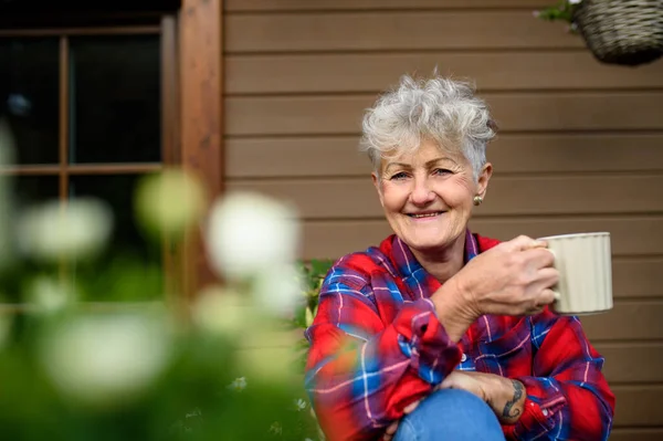 Oudere vrouw met koffie zitten op het terras in de zomer, rusten. — Stockfoto