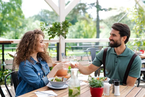 Glückliches Paar sitzt draußen auf der Terrasse Restaurant, klirrt Gläser. — Stockfoto
