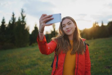 Yaz doğasında çayırda yürüyüş yapan genç bir kadın selfie çekiyor..