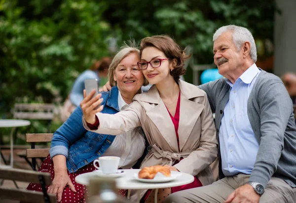 Mulher com pais idosos sentados ao ar livre no café, tirando selfie . — Fotografia de Stock