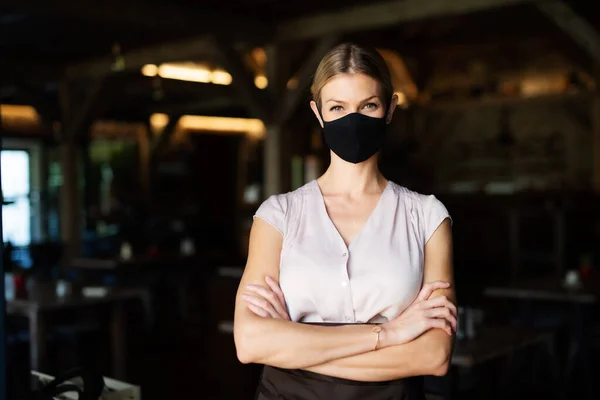Официантка в маске, стоящая в помещении на террасе ресторана, скрещенные руки . — стоковое фото