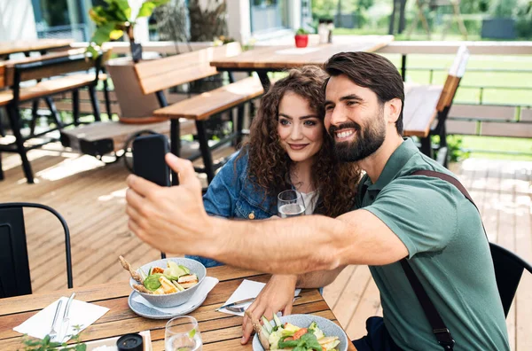 Happy couple sitting outdoors on terrace restaurant, taking selfie. — Stock Photo, Image