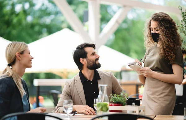 Waitress with face mask serving happy couple outdoors on terrace restaurant. — Stock Photo, Image