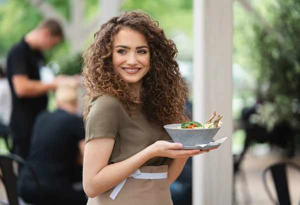 Waitress with plate standing on terrace restaurant, looking at camera. — Stock Photo, Image