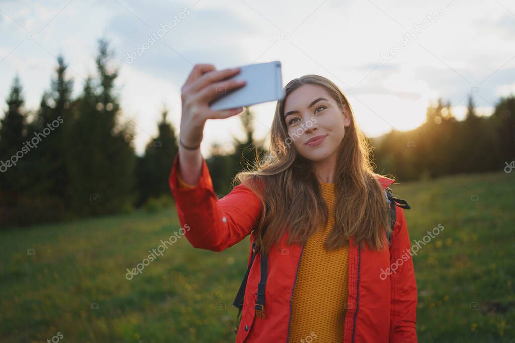 Young woman on a walk outdoors on meadow in summer nature, taking selfie.