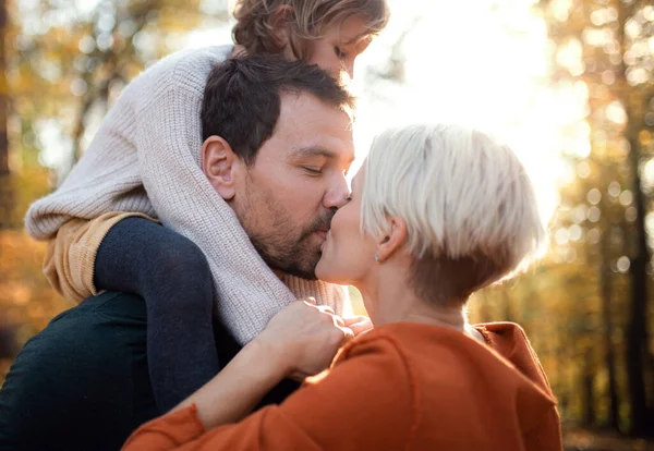 Casal jovem com filha pequena em um passeio na floresta de outono, beijando . — Fotografia de Stock
