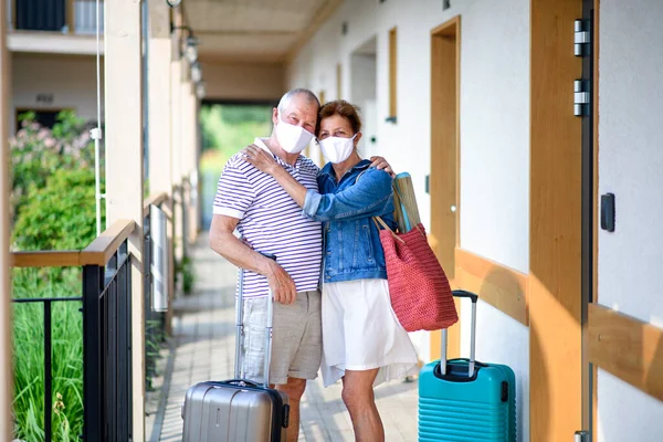 Casal sênior com máscaras faciais e bagagem fora do apartamento de férias . — Fotografia de Stock