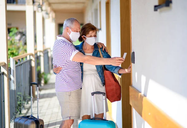 Pareja mayor con máscaras faciales y equipaje fuera del apartamento de vacaciones . — Foto de Stock