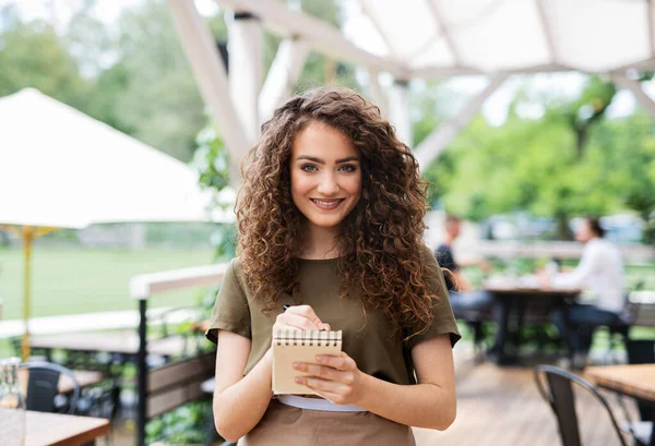 Portrait of waitress standing on terrace restaurant, holding order pad. — Stock Photo, Image