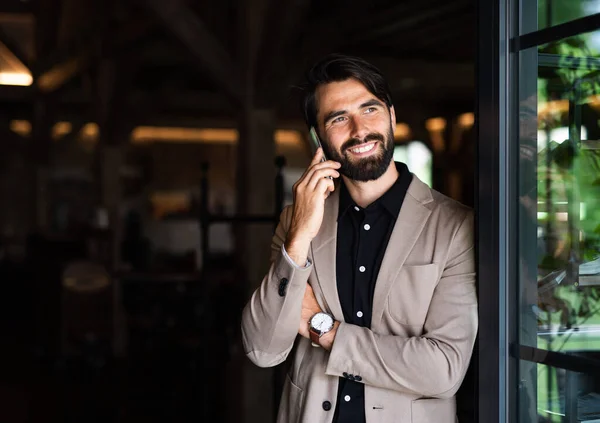 Porträtt av affärsman med jacka står inomhus i restaurang, med hjälp av telefon. — Stockfoto