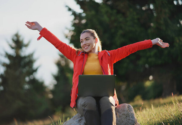 Happy young woman using laptop in summer nature, outdoor office concept.