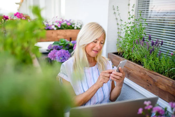 Mulher sênior ativa com laptop e smartphone trabalhando na varanda, escritório em casa . — Fotografia de Stock