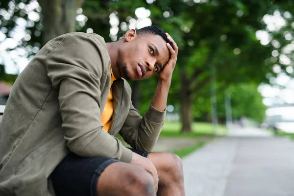 Разочарованный молодой черный мужчина сидит на скамейке на открытом воздухе в городе, черная жизнь имеет значение концепции. — стоковое фото