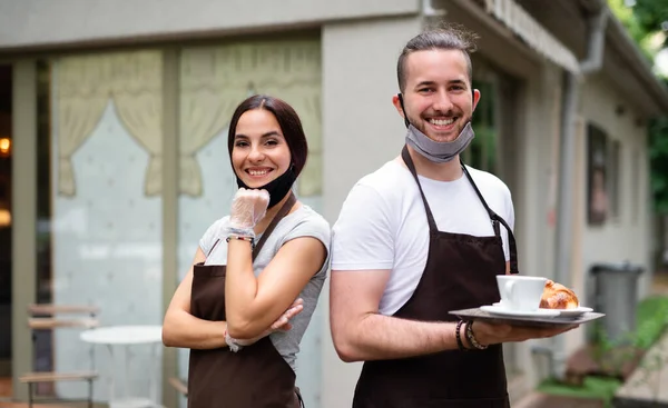 Waiter and waitress with face mask in cafe, looking at camera.