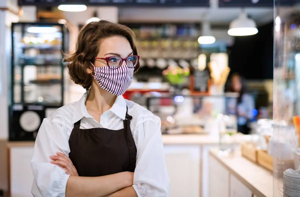 Νεαρή σερβιτόρα με μάσκα στο καφέ, σταυρωμένα τα χέρια. — Φωτογραφία Αρχείου