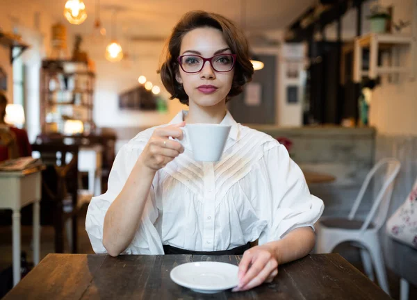 Grave giovane donna con caffè in casa in caffè, guardando la fotocamera. — Foto Stock