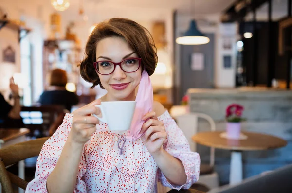 Giovane donna con maschera viso e caffè in casa in caffè, guardando la fotocamera. — Foto Stock