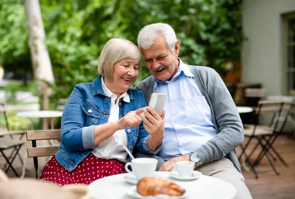 Счастливая влюбленная старшая пара сидит на улице в кафе, используя смартфон. — стоковое фото