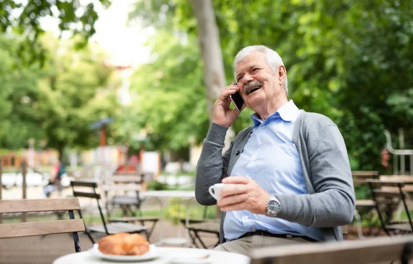 Hombre mayor con teléfono inteligente sentado al aire libre en la cafetería, haciendo una llamada telefónica . —  Fotos de Stock