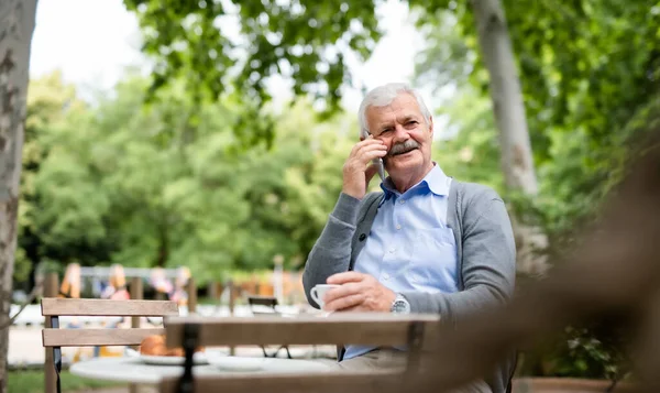 一个拿着智能手机的老人坐在外面的咖啡店里打电话. — 图库照片