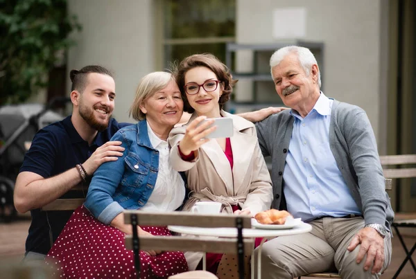 Senior par med vuxen son och dotter sitter utomhus i caféet, tar selfie. — Stockfoto