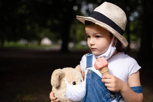 Niña pequeña con mascarilla comiendo helado al aire libre en la ciudad . — Foto de Stock