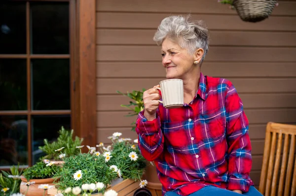 Seniorin mit Kaffee sitzt im Sommer auf Terrasse und ruht sich aus. — Stockfoto