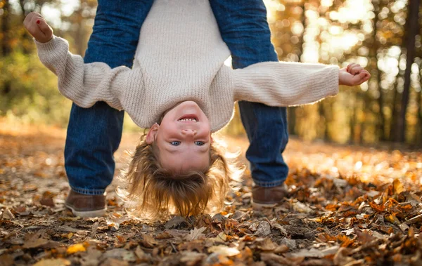 Невідомий батько тримає маленьку дочку догори ногами в осінньому лісі . — стокове фото