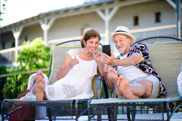 Старшая пара с вином и смартфоном на открытом воздухе в отпуске, расслабляющий. — стоковое фото