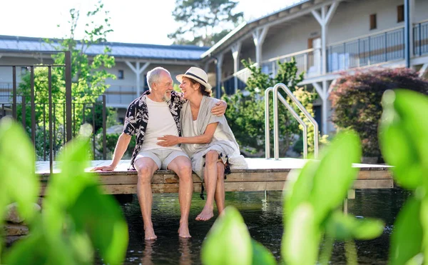 Старшая пара, сидящая на открытом воздухе у озера отеля на отдыхе, развлекаясь. — стоковое фото