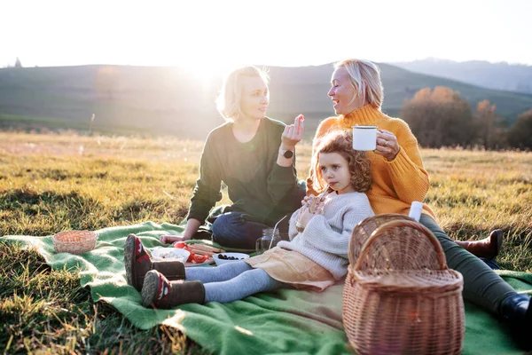 Piccola ragazza con madre e nonna che fa un picnic in natura al tramonto. — Foto Stock