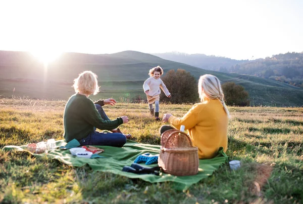 Kleines Mädchen mit Mutter und Großmutter beim Picknick in der Natur bei Sonnenuntergang. — Stockfoto