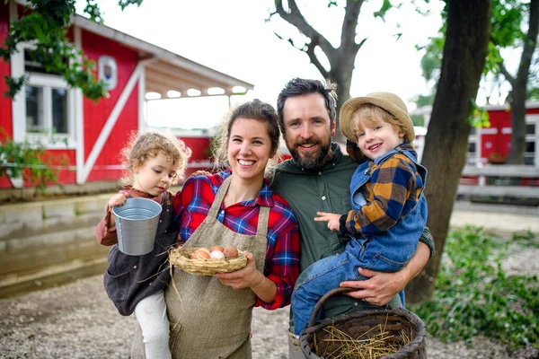 Portrait of family with small children standing on farm, holding basket with eggs. — Stock Photo, Image