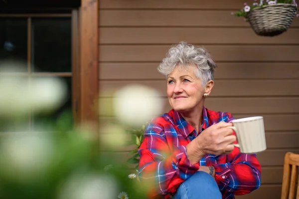 Oudere vrouw met koffie zitten op het terras in de zomer, rusten. — Stockfoto