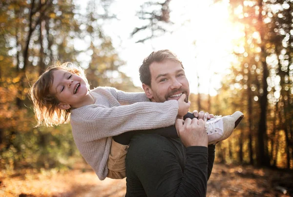 Mature father giving piggyback ride to small daughter on a walk in autumn forest. — Stock Photo, Image