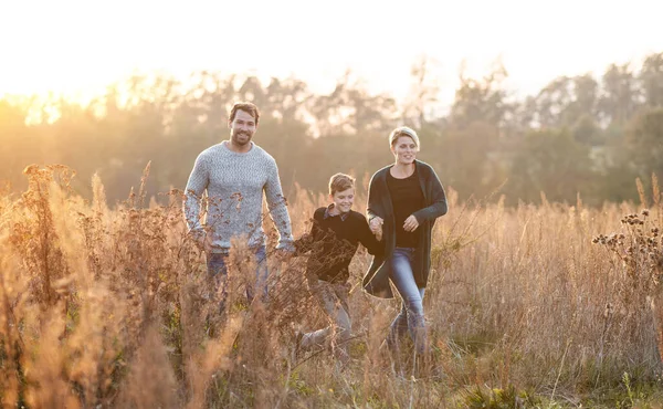 Bela família jovem com pequeno filho em um passeio na natureza de outono . — Fotografia de Stock
