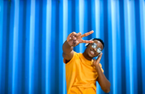 Alegre joven negro de pie sobre fondo azul, concepto de gesto de paz. — Foto de Stock