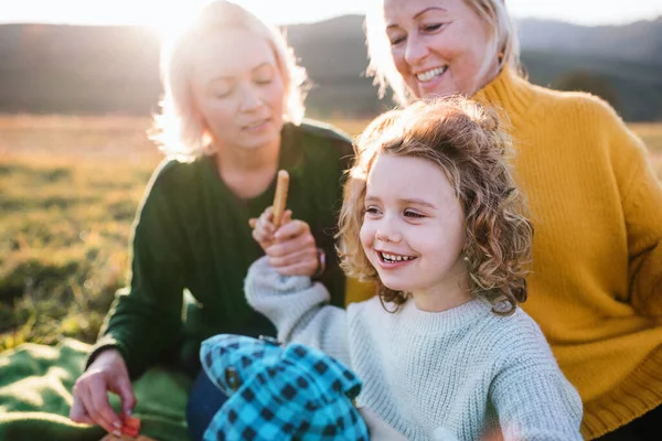 Gadis kecil dengan ibu dan nenek memiliki piknik di alam saat matahari terbenam. — Stok Foto