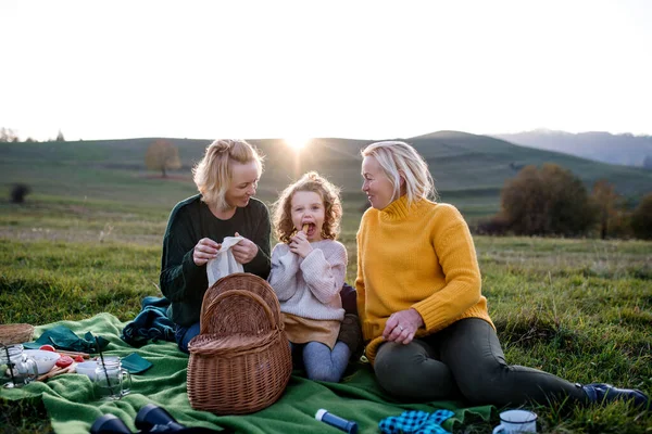 Malá dívka s matkou a babičkou mají piknik v přírodě při západu slunce. — Stock fotografie