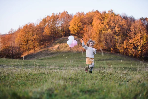 Glada liten flicka med ballonger i höst natur. — Stockfoto