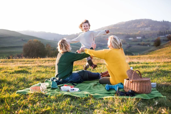 Mała dziewczynka z matką i babcią mają piknik w przyrodzie o zachodzie słońca. — Zdjęcie stockowe