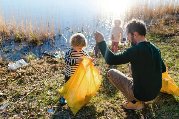 Vader met kleine kinderen verzamelen van afval buiten in de natuur, plogging concept. — Stockfoto
